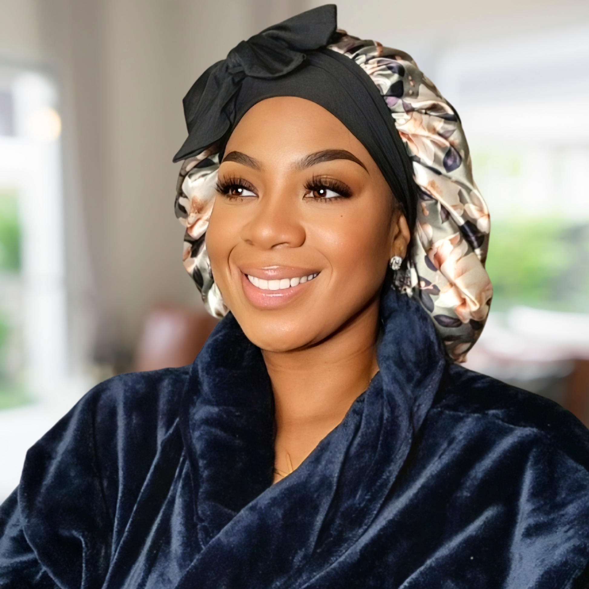 Beautiful African American model wearing an olive green floral stretch tie bonnet in a blurred background in a plush navy blue robe