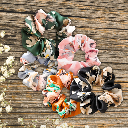 floral satin scrunchies on a wooden plank background in the colors, Evergreen Petals, Peach Blossom, Sky Blossom, Amber Bloom, and Midnight Bloom.