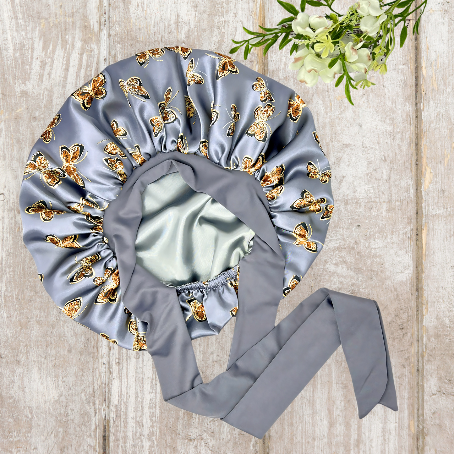 Beautiful stretch tie gray butterfly printed satin lined satin hair bonnet on a light wood background
