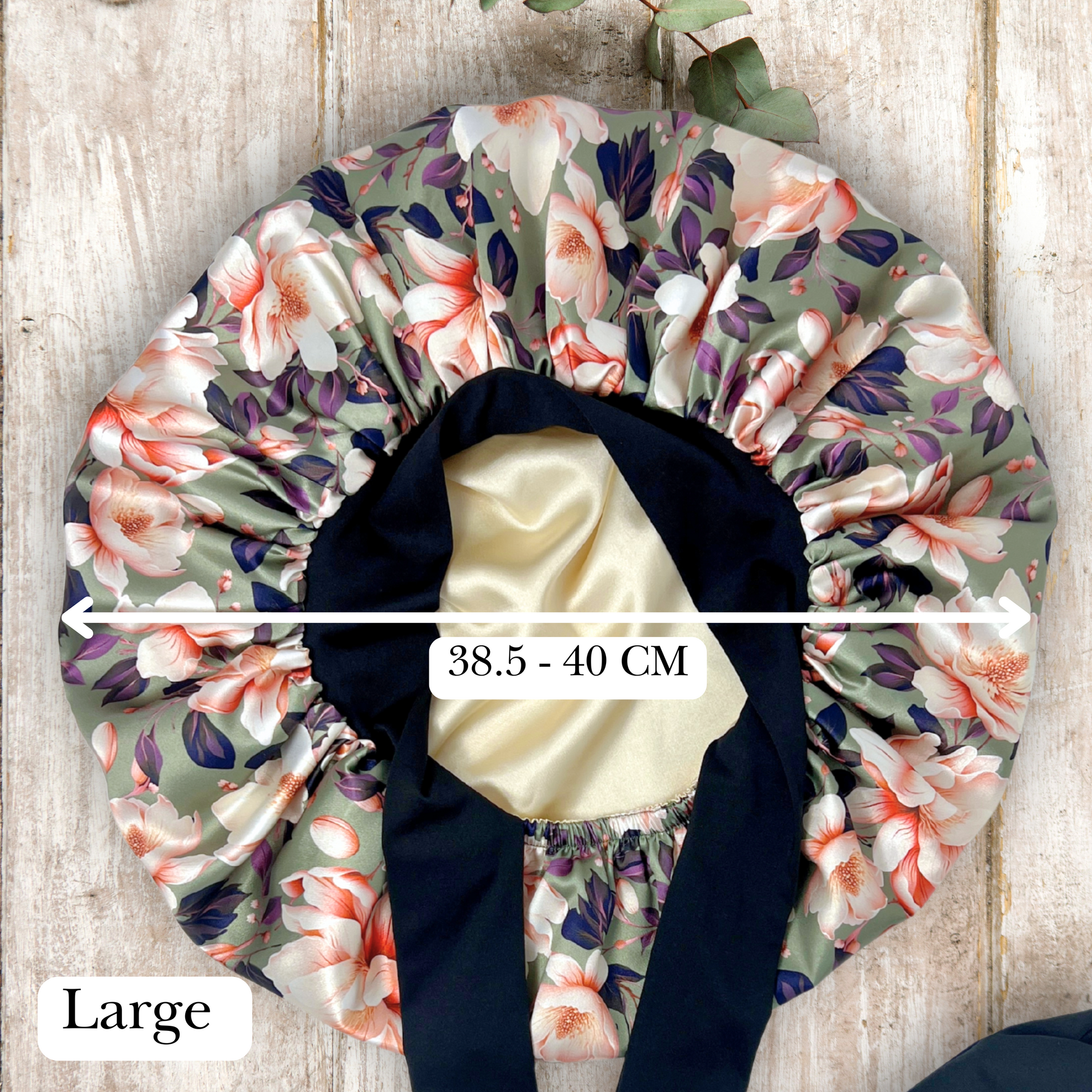 Elegant olive colored satin bonnet with a floral print, featuring a black stretch tie band for a secure and stylish fit, displayed on a wooden background.