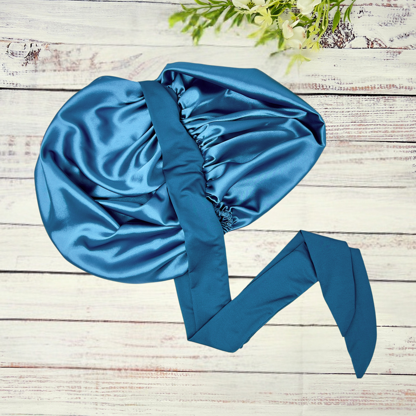 Peacock blue satin hair bonnet displayed on a light wood background, showcasing smooth satin texture and vibrant color. Ideal for curly, natural, and protective hairstyles.