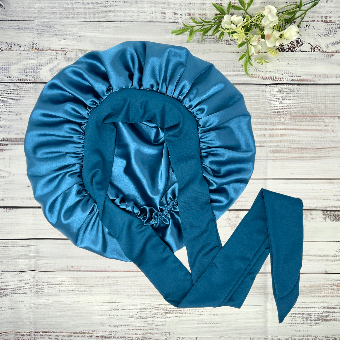 Peacock blue stretch tie satin hair bonnet displayed on a light wood background, showcasing smooth satin texture and vibrant color. Ideal for curly, natural, and protective hairstyles.