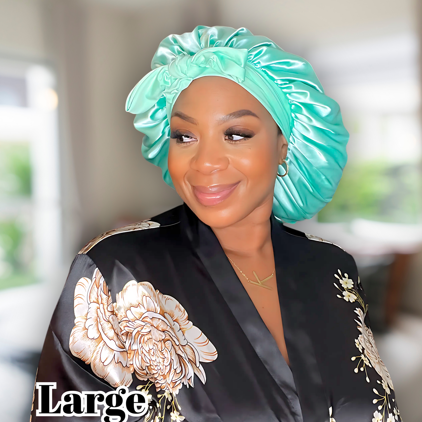 Africa American woman modeling large aqua green stretch tie bonnet in a blurred living room.