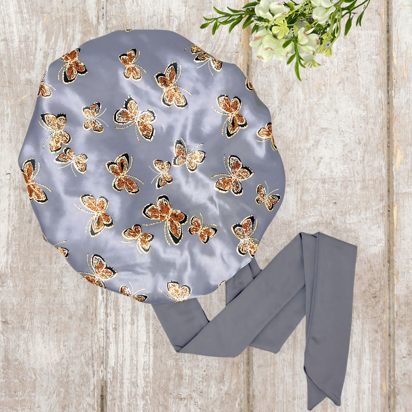 Beautiful stretch tie gray butterfly printed satin lined satin hair bonnet on a light wood background