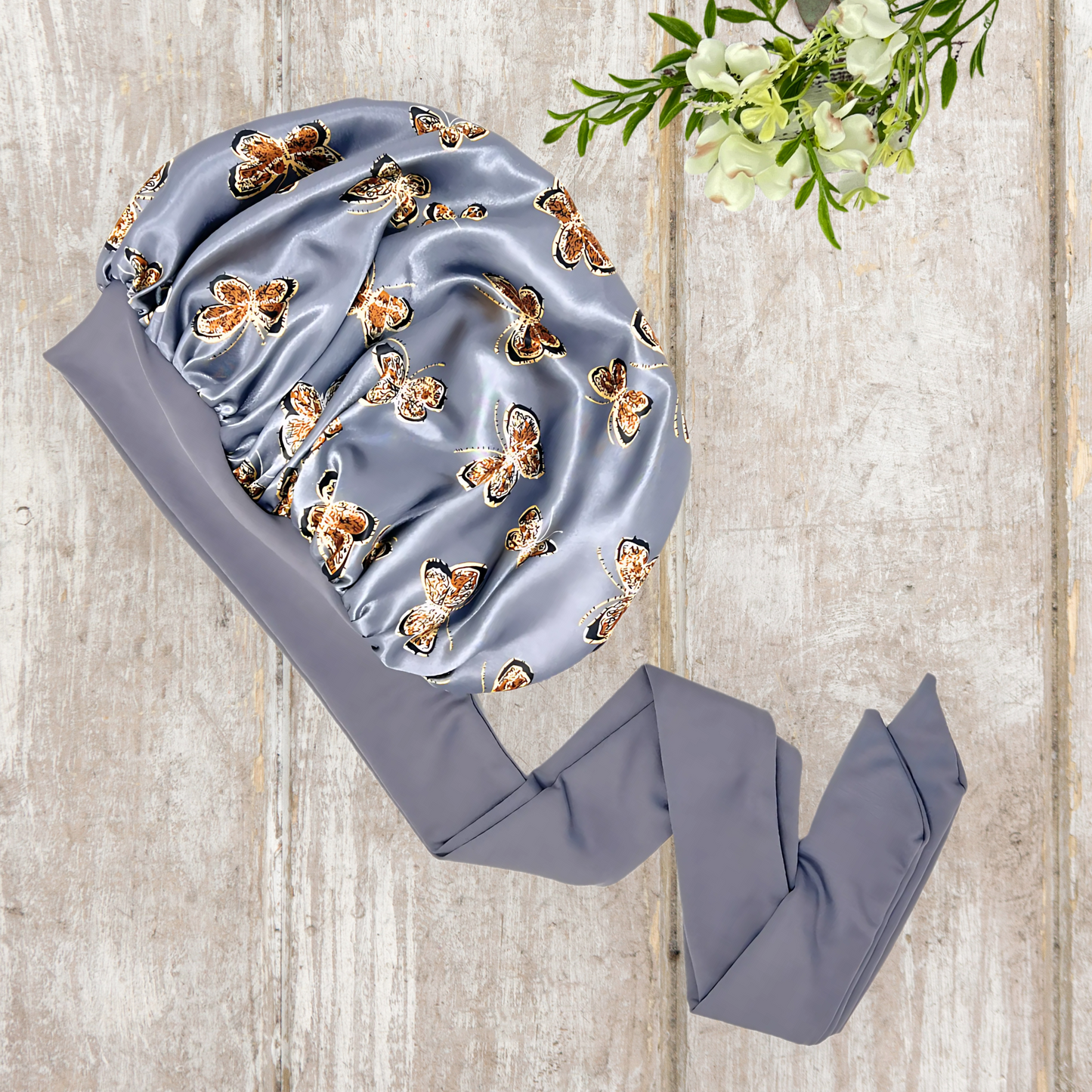 Beautiful stretch tie gray butterfly printed satin lined satin hair bonnet on a light wood background