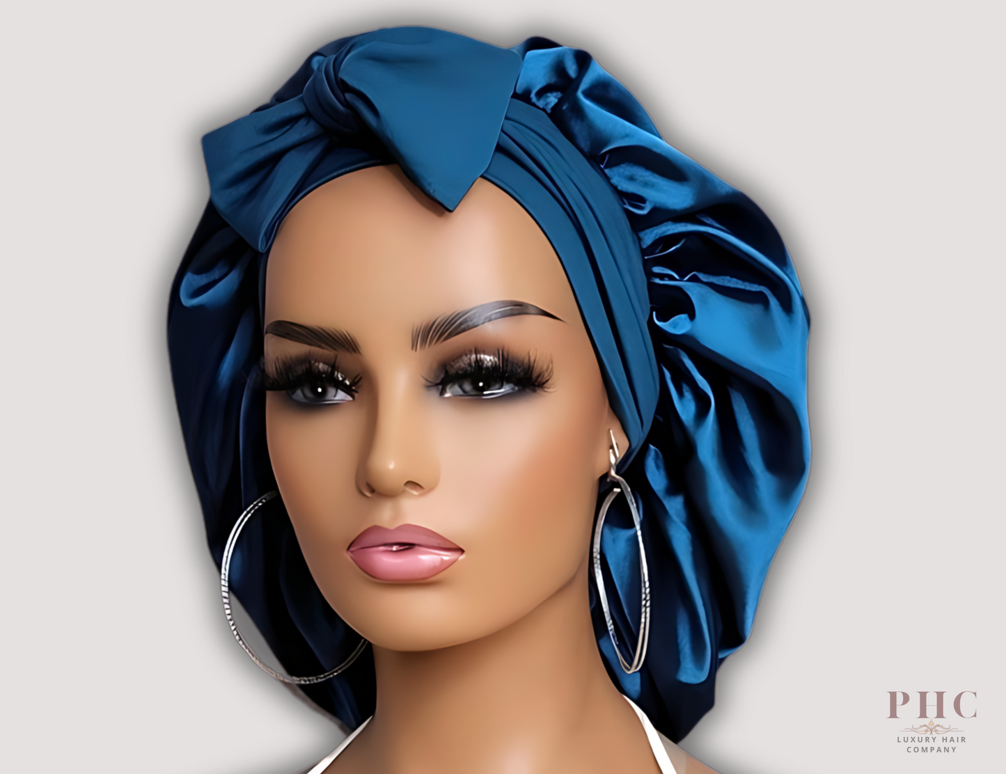 Beautiful tanned Caucasian mannequin wearing a midnight blue satin hair bonnet on a gray background.