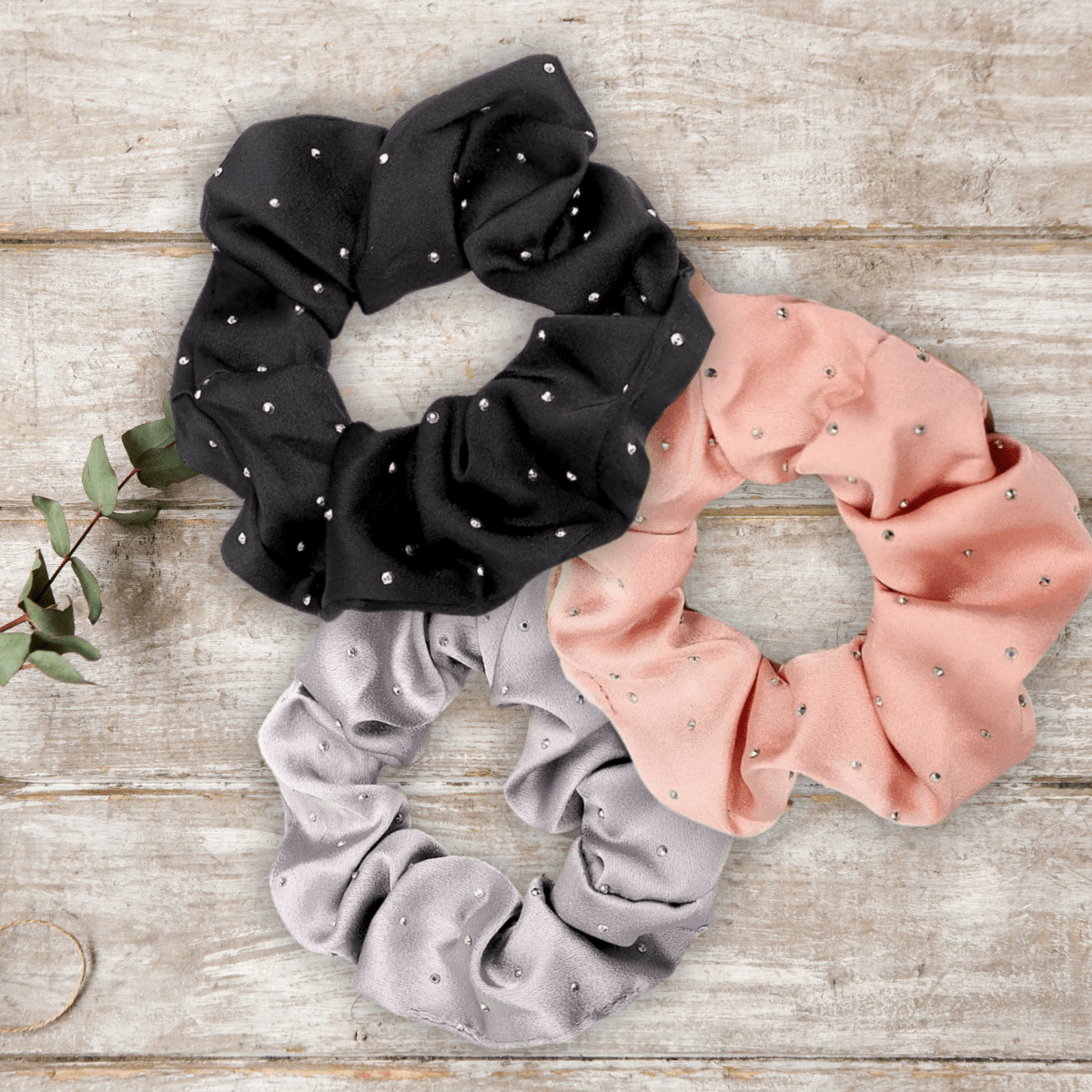 Black, pink, and gray scrunchies with small sparkly rhinestone embellishments on a wooden surface.