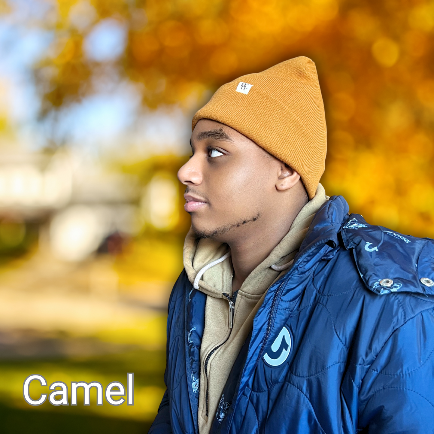 African American male modeling a PHC Prince Hair Company satin lined beanie in the color camel on a blurred out fall background.
