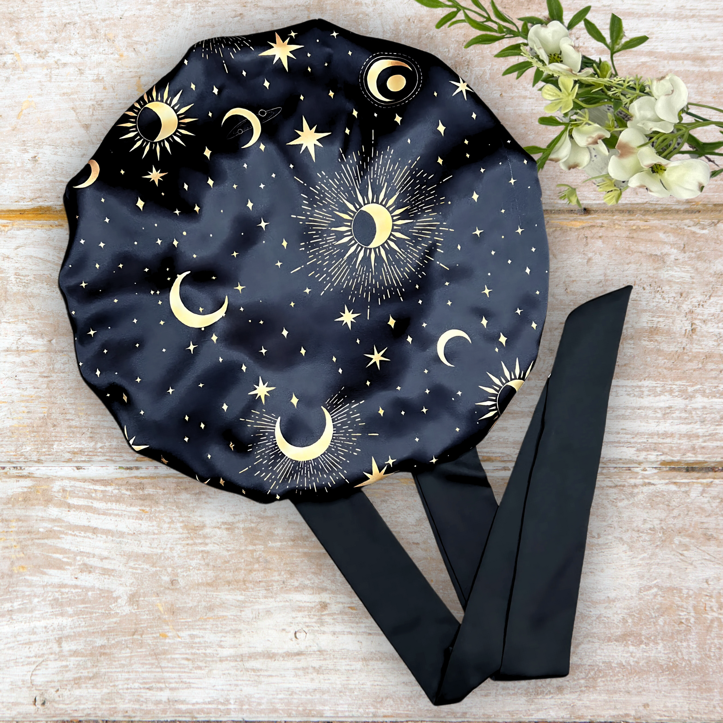 Satin Lined Bonnet in Custom PHC Starry Print with adjustable stretch ties in small on a wooden background. Perfect silky satin sleep cap for protecting your hair throughout the night.