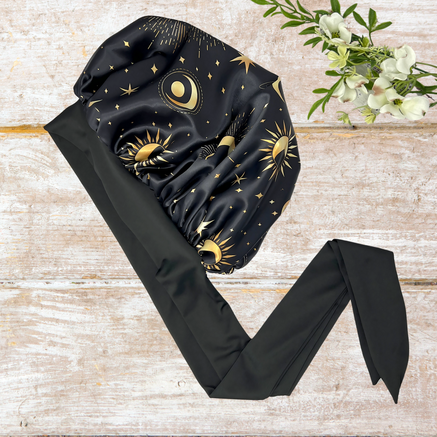 Satin Lined Bonnet in Custom PHC Starry Print with adjustable stretch ties in small on a wooden background. Perfect silky satin sleep cap for protecting your hair throughout the night.