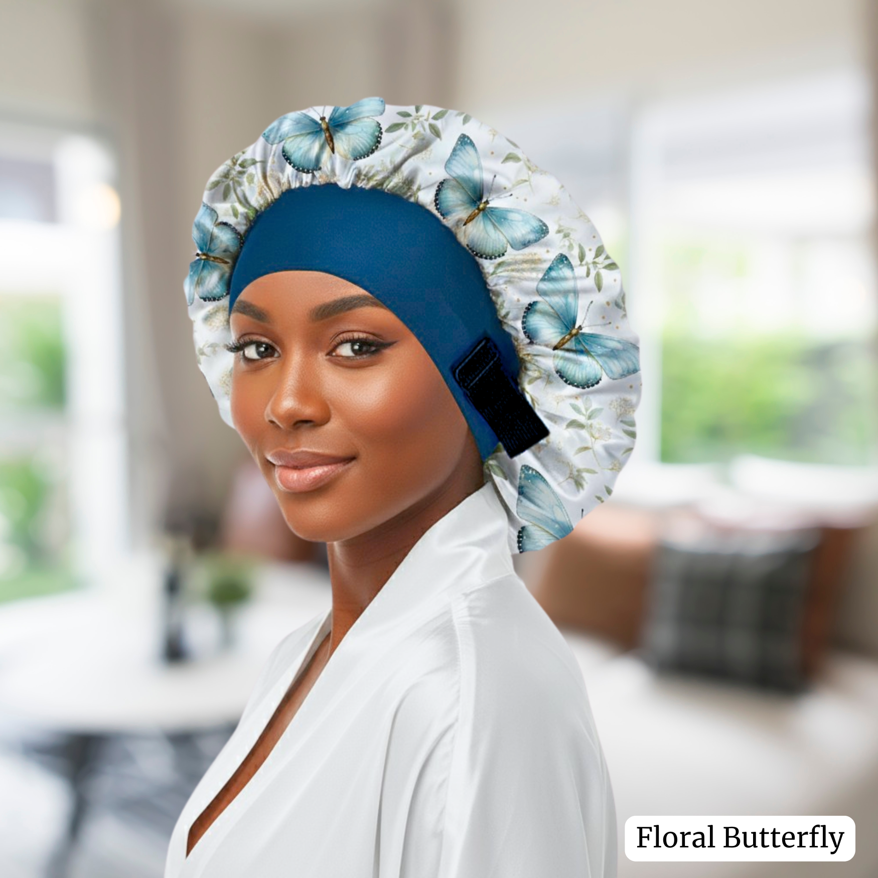 Woman wearing a Charmeuse silk satin no-slip wide band hair bonnet in a floral butterfly print, featuring a deep peacock blue band and a close-up of the adjustable elastic pull, showing the secure, edge-friendly fit for protective nighttime hair care in a blurred indoor setting.