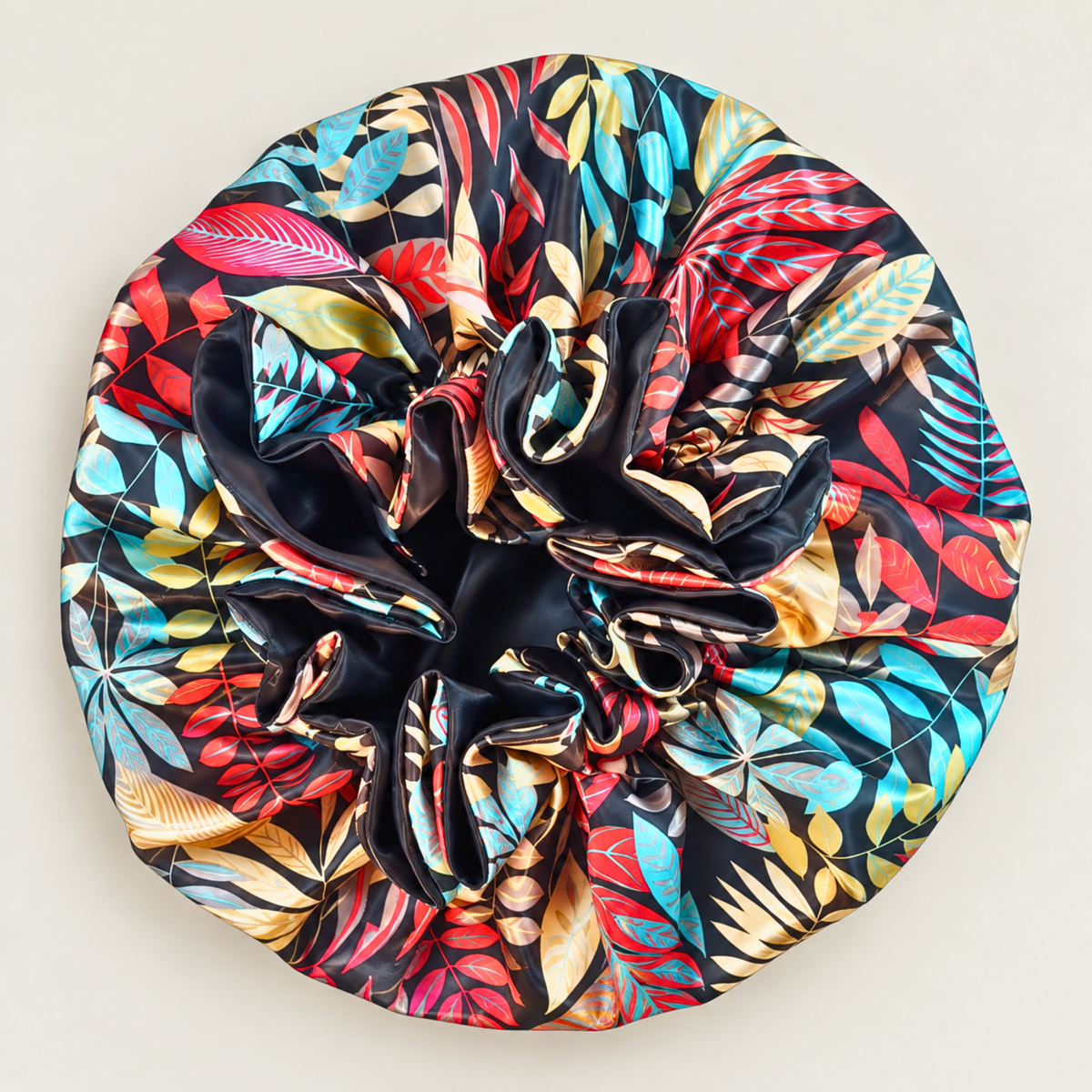 Black Autumn ruffle satin bonnet laid flat, black with a multicolor tropical leaf print
