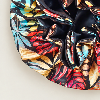Close-up of the Black Autumn ruffle satin bonnet, black with red, yellow and blue leaf print