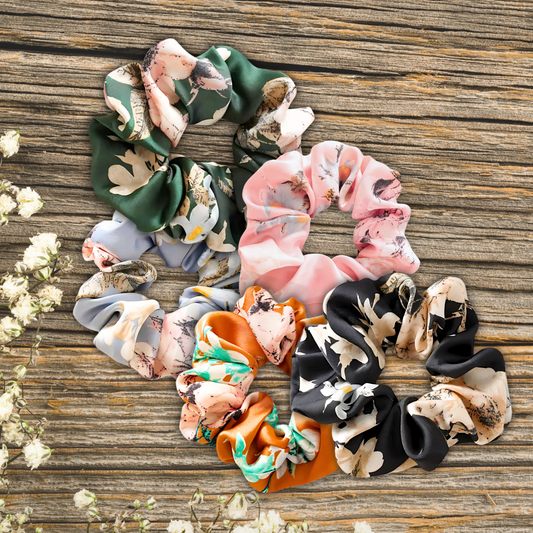 floral satin scrunchies on a wooden plank background in the colors, Evergreen Petals, Peach Blossom, Sky Blossom, Amber Bloom, and Midnight Bloom. 