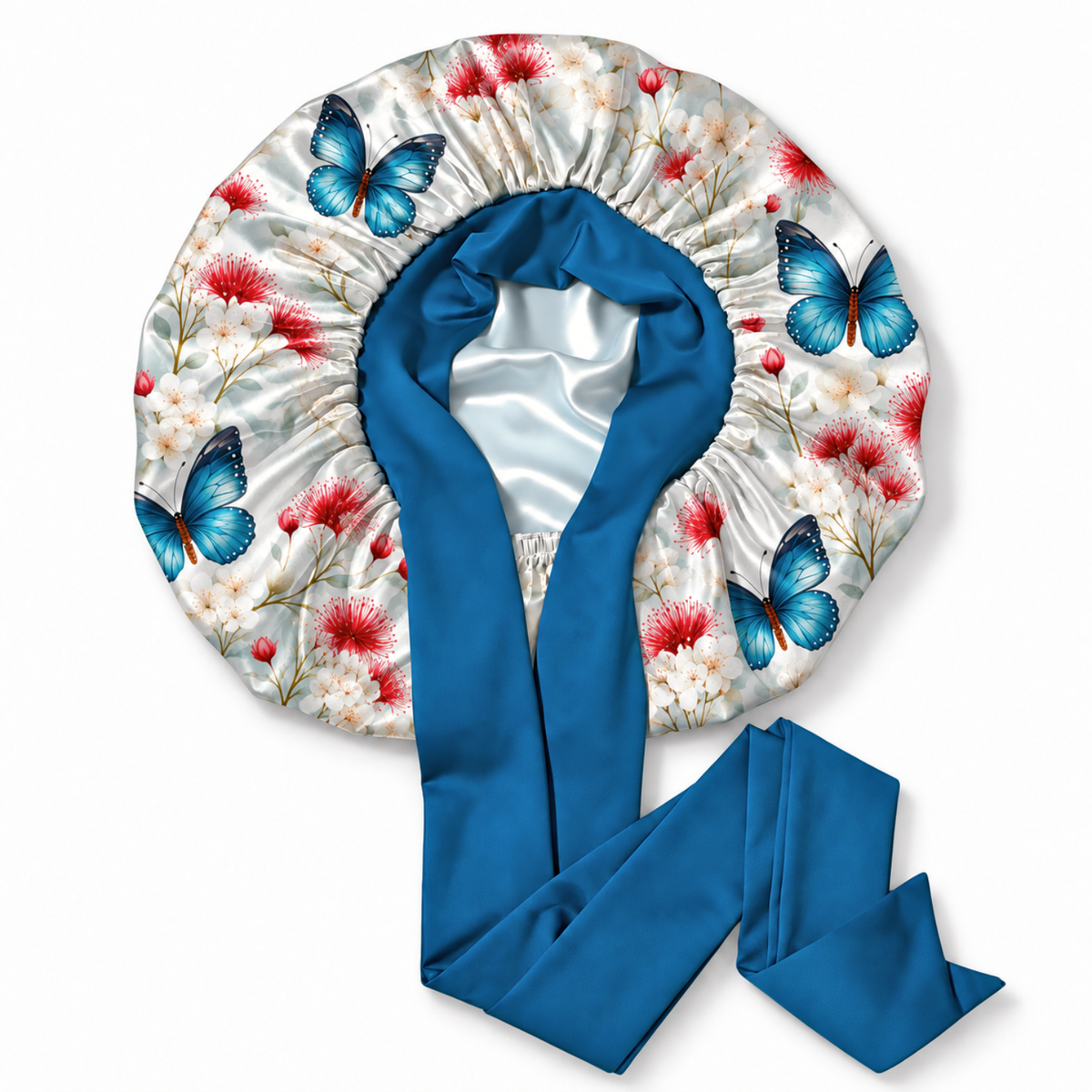 A satin sleep bonnet with a blue satin neck strap, featuring a white satin body printed with blue butterflies and red and white flowers, shown on a plain white background.