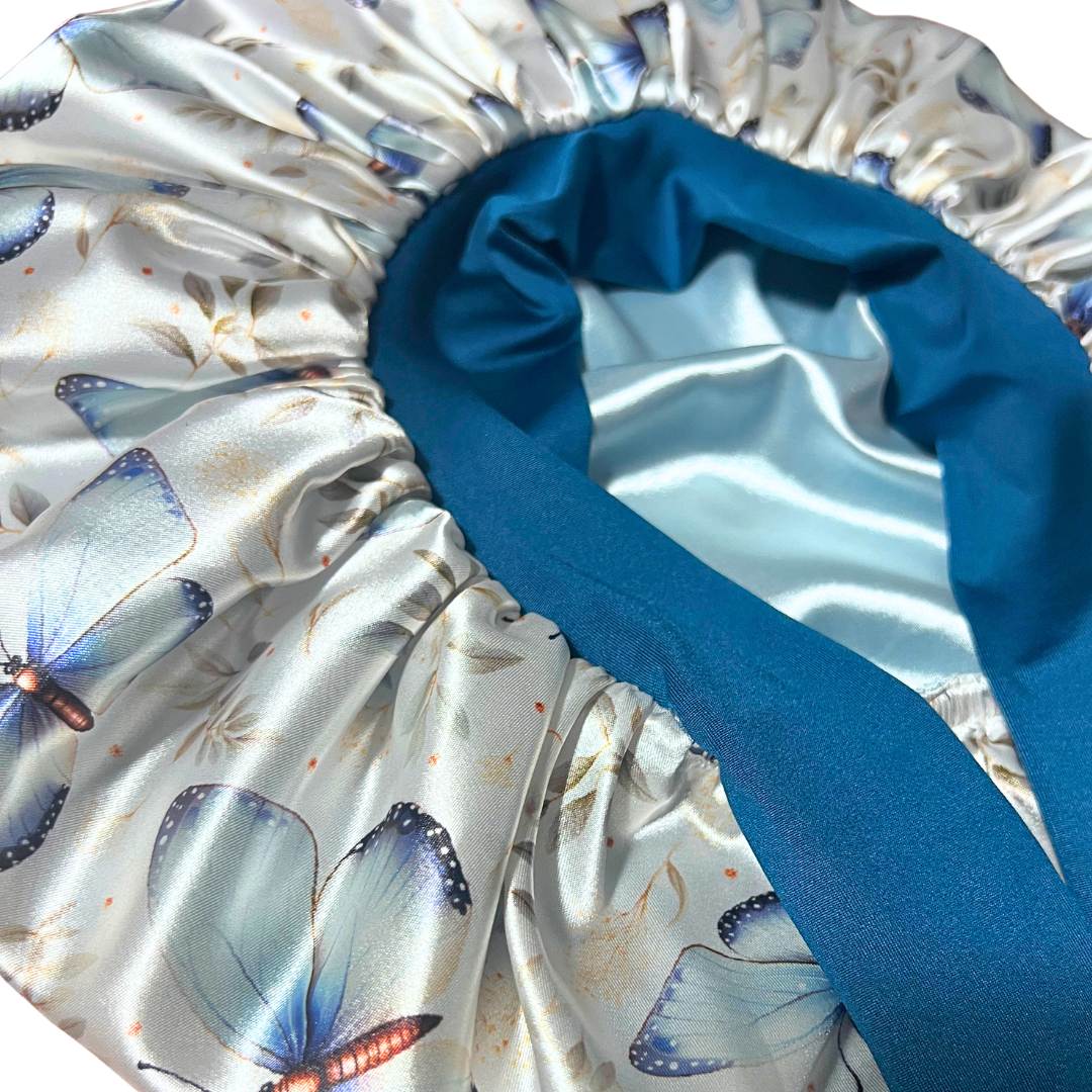 Close-up of a satin sleep cap or bonnet with a butterfly print on the exterior and a solid teal blue inner lining.