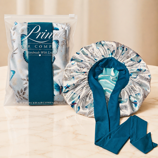 Prince Hair Company satin hair bonnet with a blue floral print and a teal satin tie, shown next to its clear plastic packaging on a light marble surface.