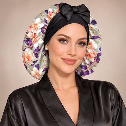 Olive Magnolia silk-blend satin bonnet with stretch ties, large size – front view of the floral print with black bow, worn with a black satin robe