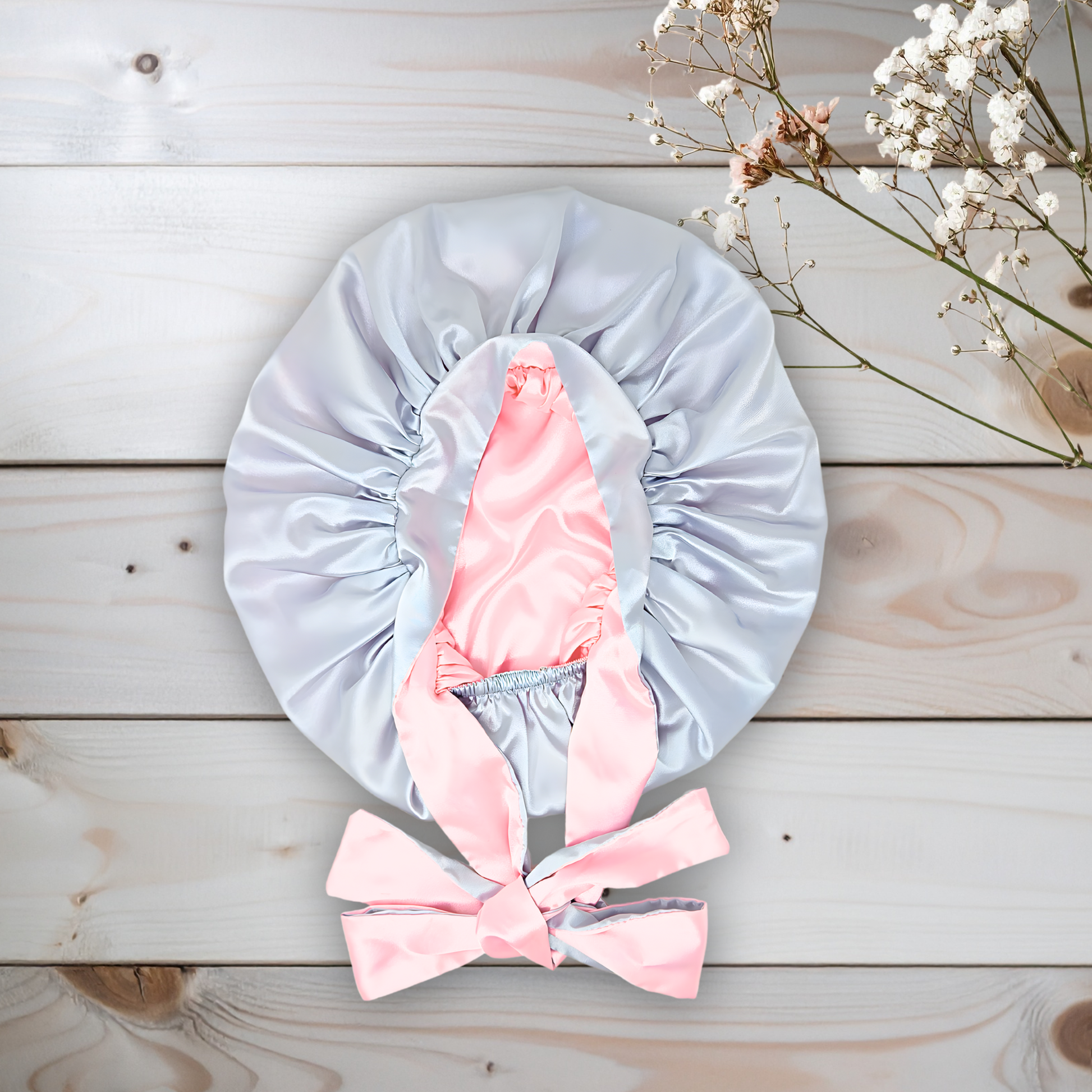 Beautiful Gray  satin bonnet with pink interior and bow on a wooden surface with white flowers.