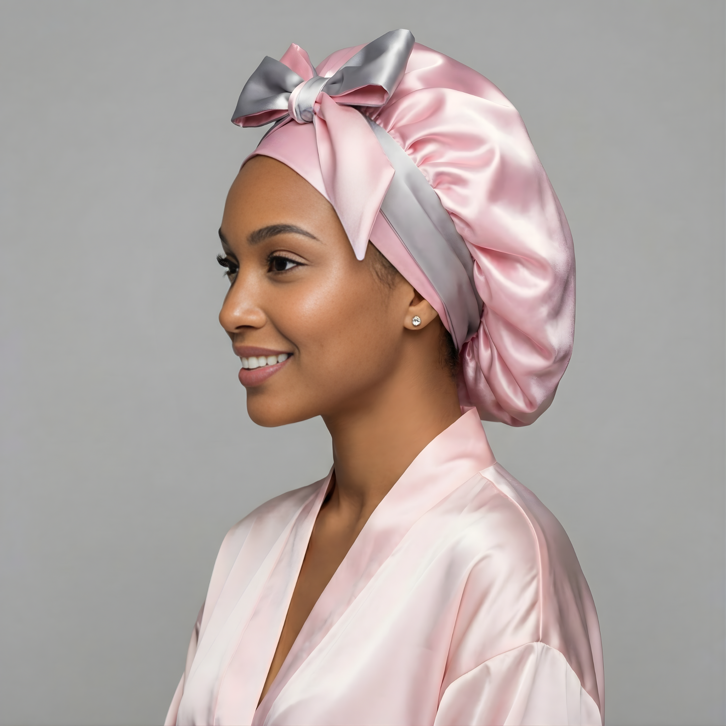 Woman wearing a pink and gray charmeuse silk satin bonnet with a gray bow against a gray background