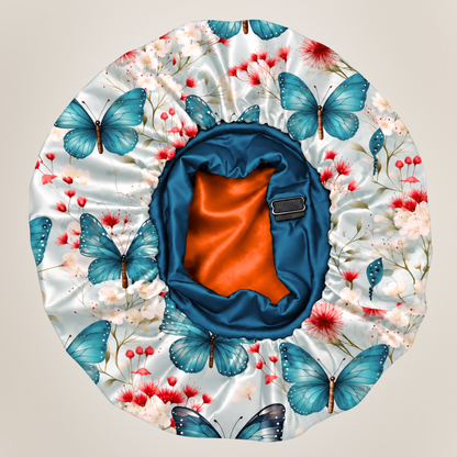 A satin sleep cap with a floral and butterfly print on a light background, featuring a blue satin trim and a bright orange inner lining.