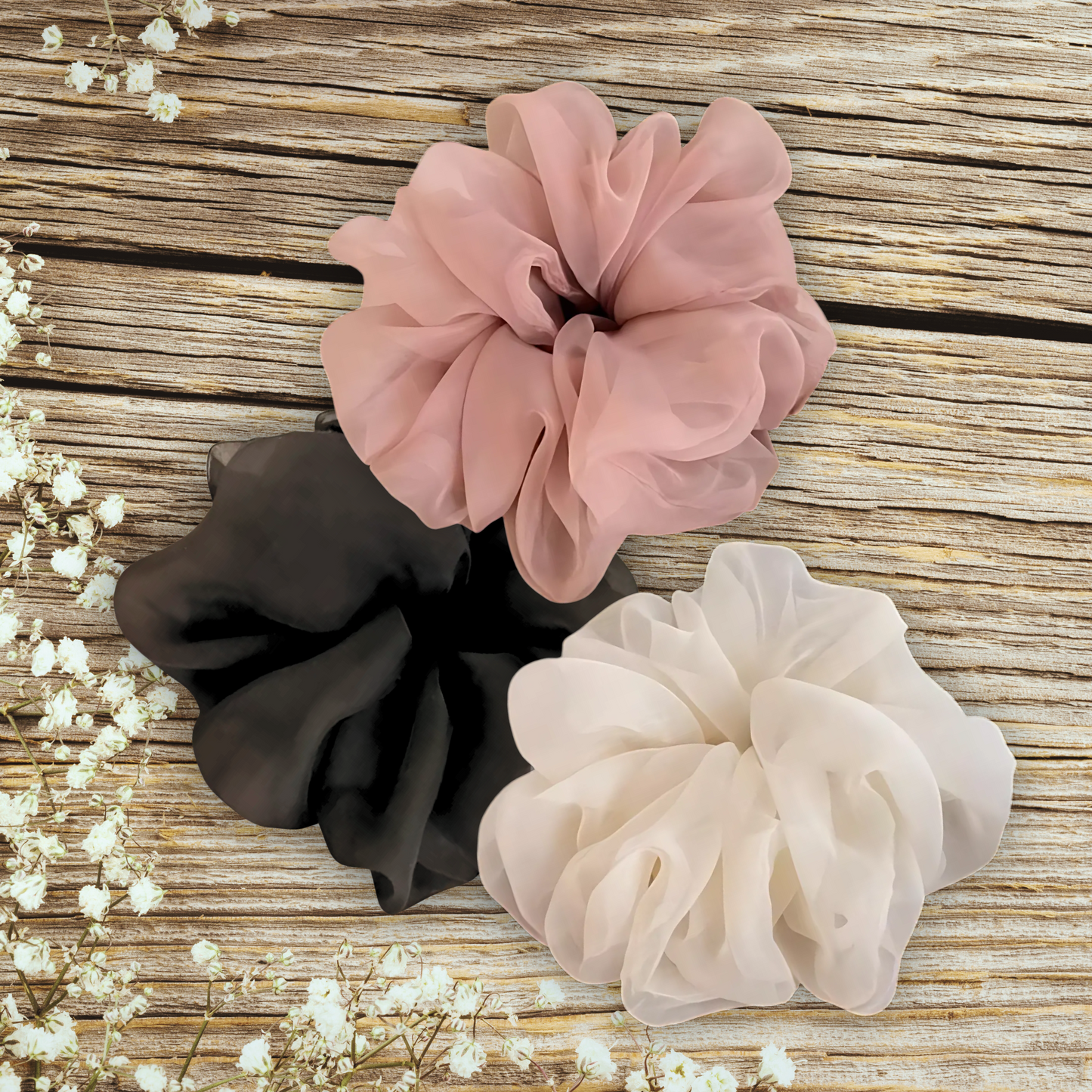 Oversized chiffon scrunchies in black, pink, and beige displayed on a wooden table, perfect for elegant hairstyles and versatile hair accessories.