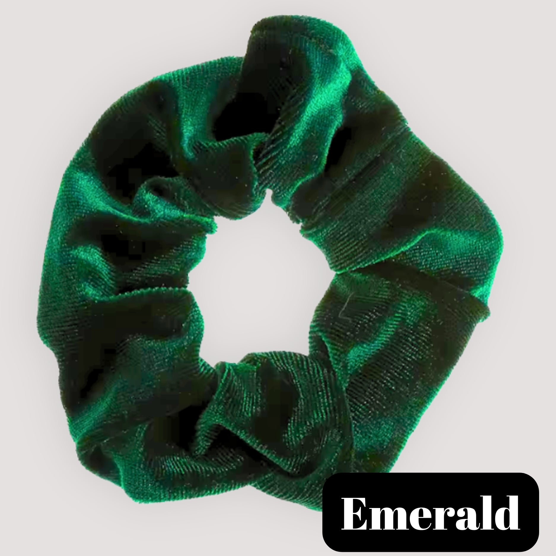 A single Emerald green handmade velvet scrunchie for damage-free hair styling on a light background, featuring a black label reading 'Emerald'.