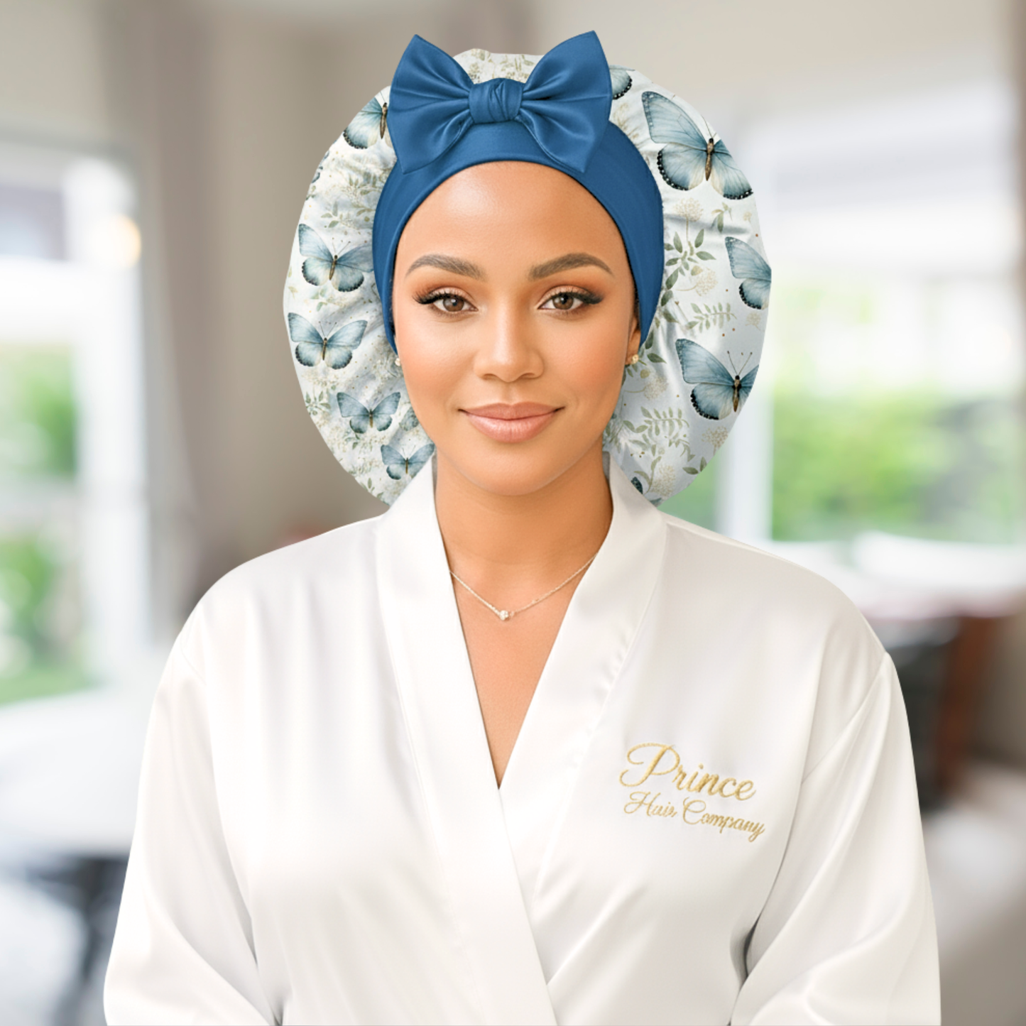 A woman wearing a butterfly floral-patterned charmeuse satin silk hair bonnet with long stretch ties formed into a bow. She is in a softly lit indoor setting with a blurred background, highlighting the bonnet’s elegant shine and handmade quality. This luxury satin sleep cap protects natural, curly, and textured hair while maintaining a cute, comfortable fit.