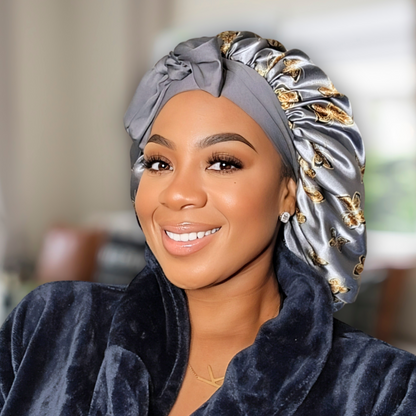 Beautiful woman modeling a stretch tie gray butterfly printed satin lined satin hair bonnet in a blurred living room. 
