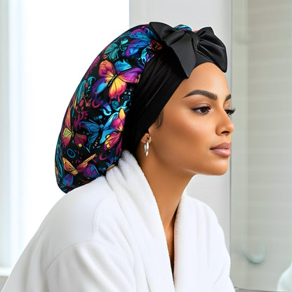 A woman wearing a colorful butterfly-patterned headscarf with a black bow, sitting in a bright modern bathroom. The soft lighting highlights the scarf’s silky texture and vibrant design. This handmade satin head wrap is perfect for protecting natural, curly, or straight hair while adding a stylish, elegant touch to a daily self-care routine.