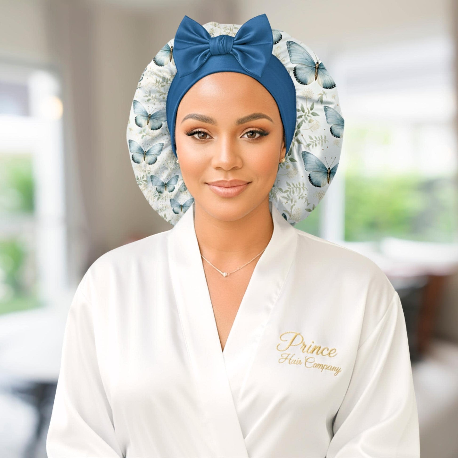A woman wearing a butterfly floral-patterned charmeuse satin silk hair bonnet with long stretch ties formed into a bow. She is in a softly lit indoor setting with a blurred background, highlighting the bonnet’s elegant shine and handmade quality. This luxury satin sleep cap protects natural, curly, and textured hair while maintaining a cute, comfortable fit.
