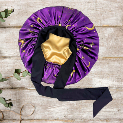 Flat lay of the reversible Celestial Plum bonnet showing the purple sun and moon print exterior with gold satin lining.