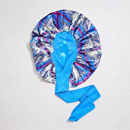 Blue paisley damask satin stretch-tie bonnet with bright blue lining laid flat on a neutral background, showing the adjustable tie design.