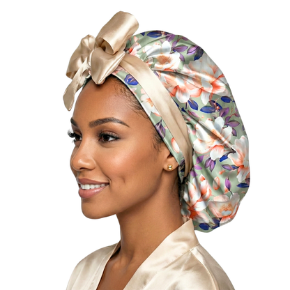 profile view of a Woman wearing a reversible olive magnolia floral print satin hair bonnet with a large champagne colored bow on a white background. Great for all hair types