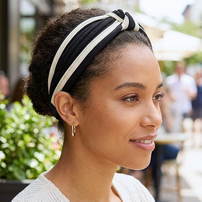 Woman outdoors wearing a black and cream twisted knot headband with textured hair pulled into a bun, side view.