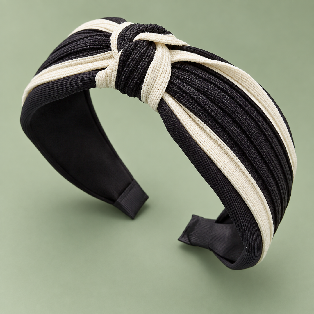 Black and cream two-tone twisted knot headband at an angle on a sage green background.