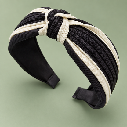 Black and cream two-tone twisted knot headband at an angle on a sage green background.
