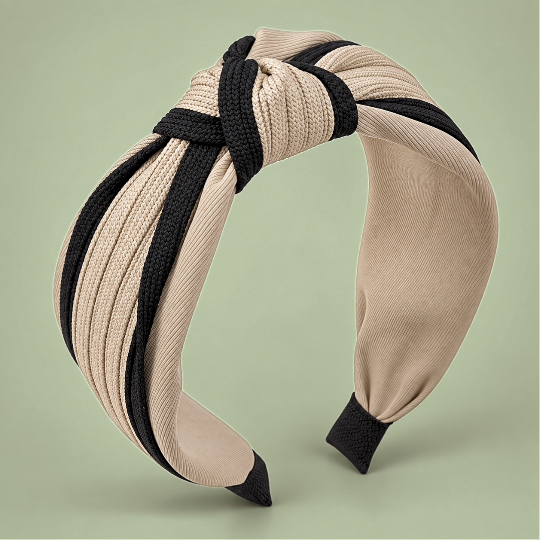 Beige and black twisted knot headband front view on sage green, showing its striped outer fabric and padded inner band.