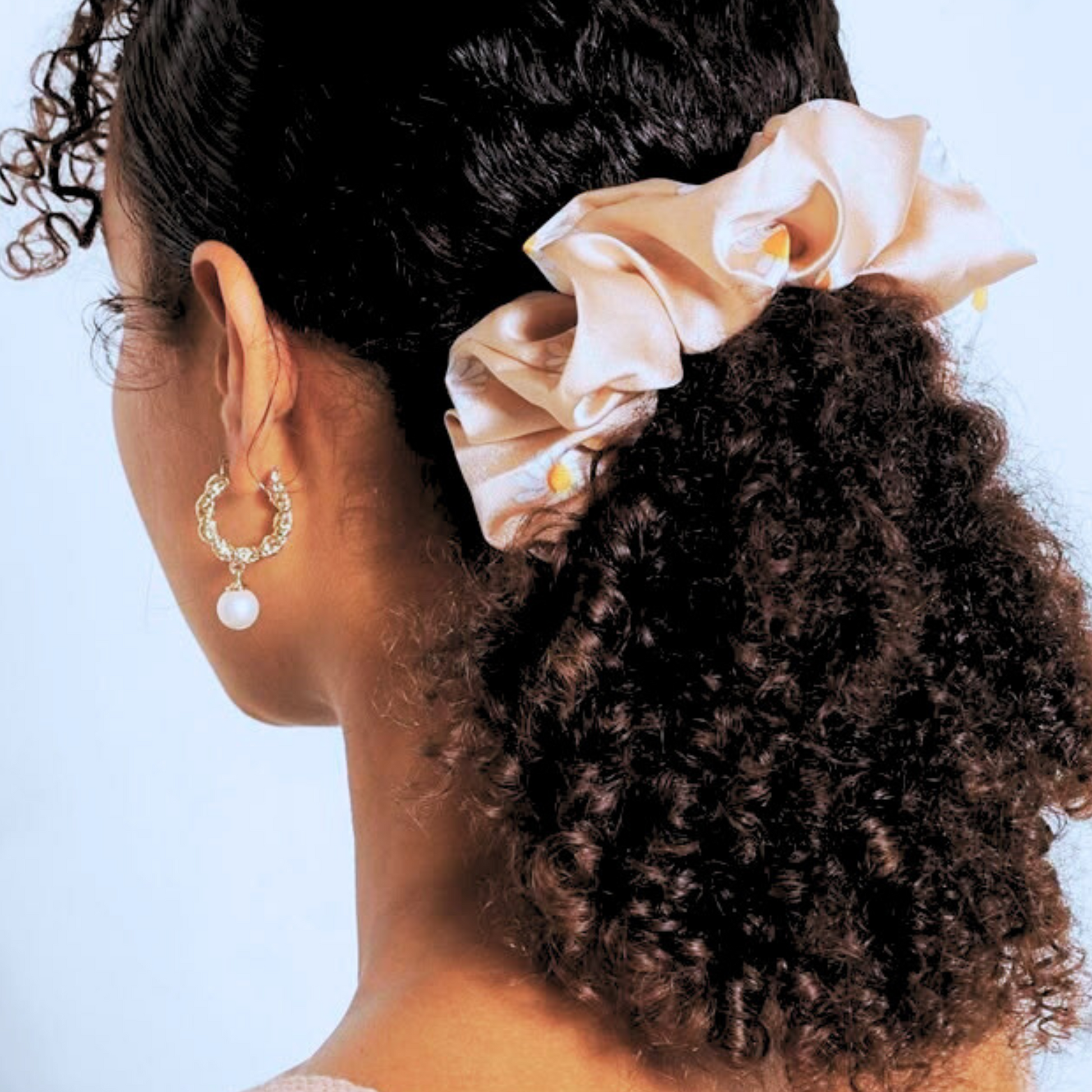 curly hair girl wearing a champagne colored hair scrunchie around her full  afro curly ponytail