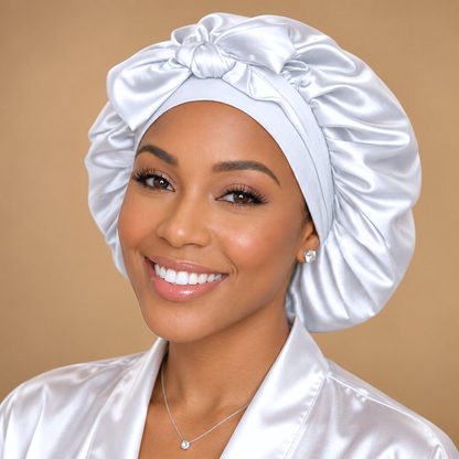 Front view of a small white satin bonnet with matching bow