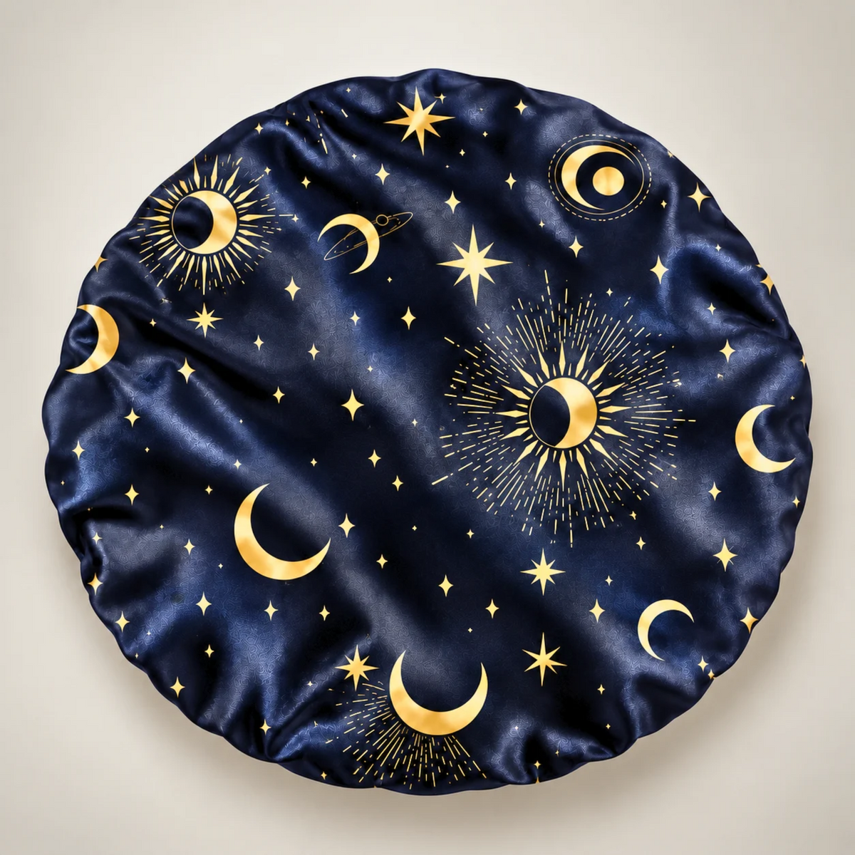 back side of a round satin bonnet featuring a celestial pattern of gold crescent moons, stars, and sunburst designs on a deep navy blue background, shown against a light beige background.