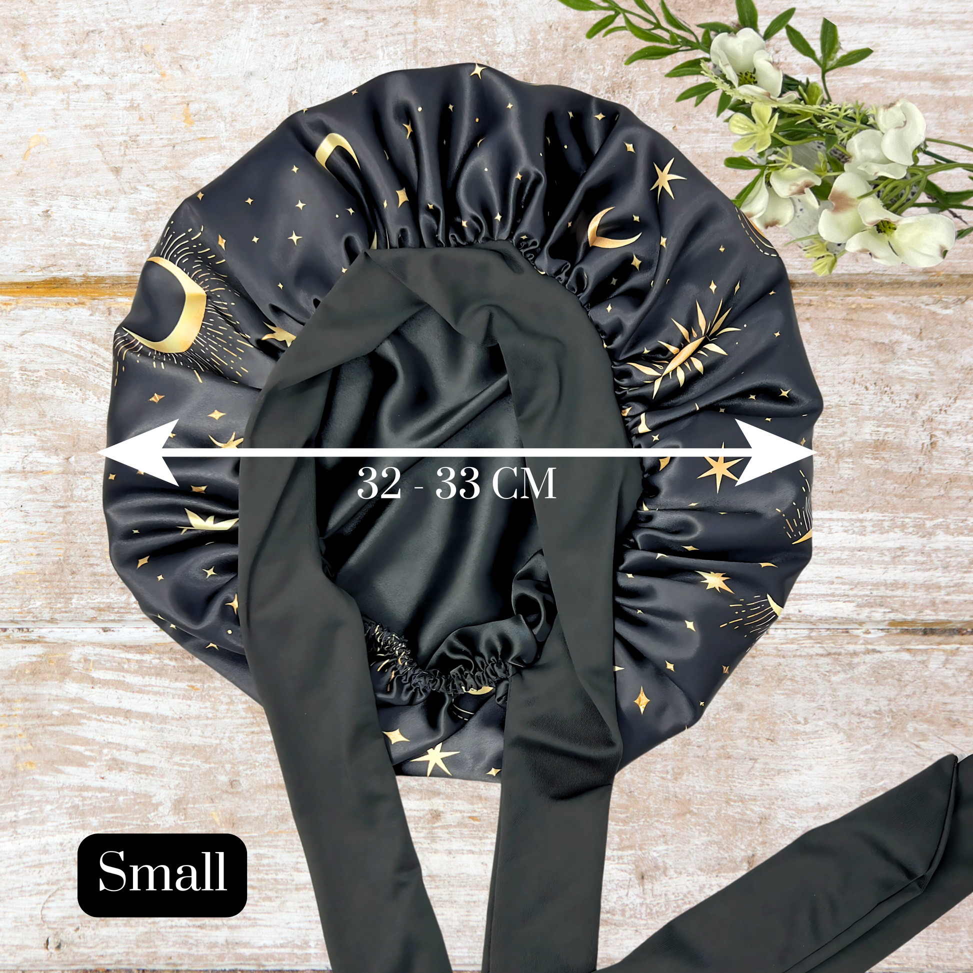 Satin Lined Bonnet in Custom PHC Starry Print with adjustable stretch ties in small on a wooden background. Perfect silky satin sleep cap for protecting your hair throughout the night. 