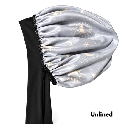 A satin bonnet with a celestial print of gold suns, moons, and stars on a light gray background, featuring a black elastic band and long black ties, shown against a white background with the text 'Unlined' in the bottom right corner.