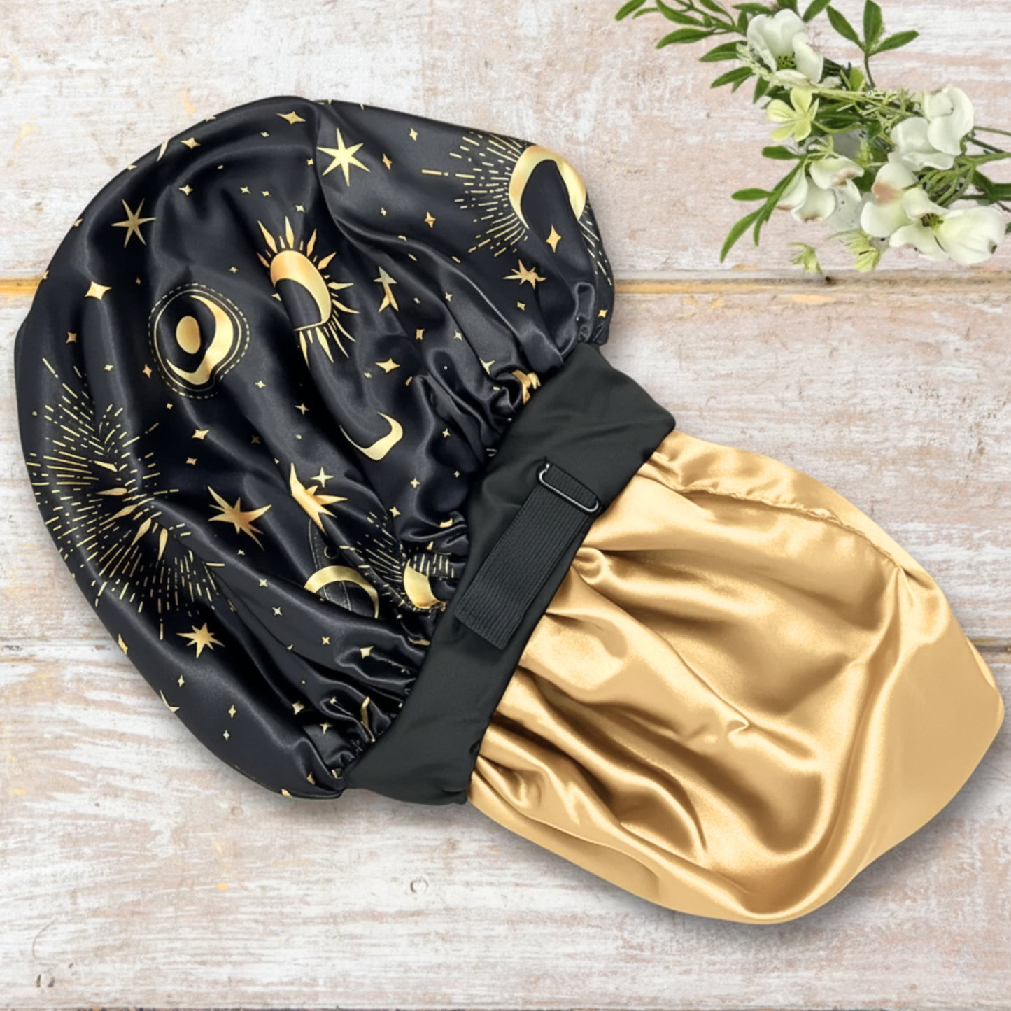 Side view of adjustable satin hair bonnet in Starry Night print and black, showing wide elastic band and smooth satin texture for curly, natural, and protective hairstyles on wood background. Pretty star, moon, celestial print for nighttime wear.