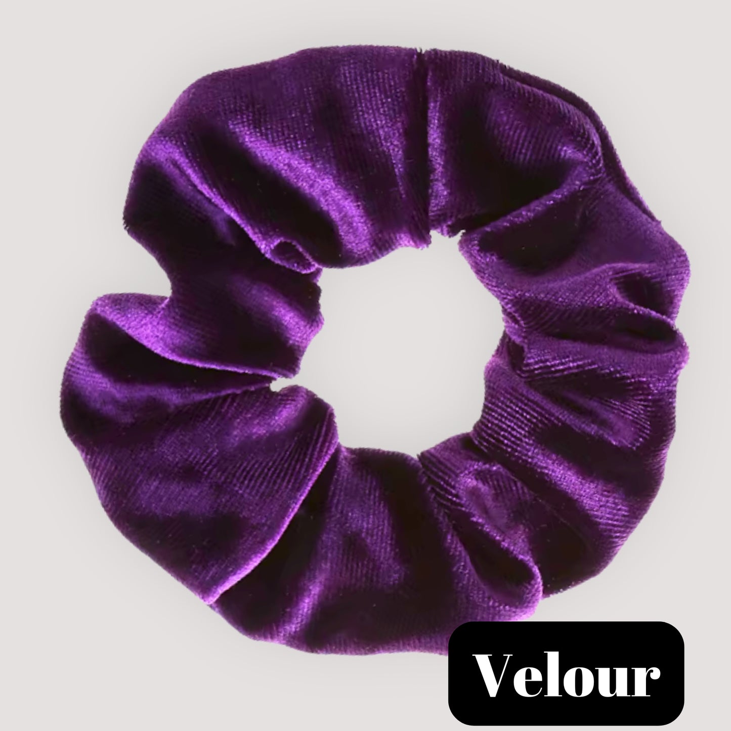A single Velour dark purple handmade velvet scrunchie for damage-free hair styling on a light background, featuring a black label reading 'Velour.'